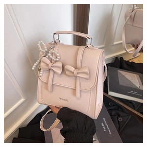 Detail of pink leather handbag featuring elegant bows and a decorative white pearl charm