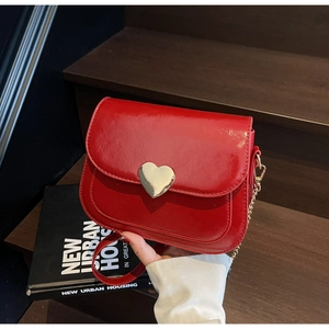 Detail of red glossy square bag featuring a gold heart buckle on a wooden staircase