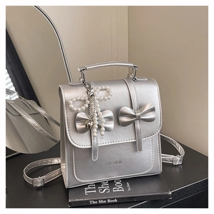 Detail of silver backpack featuring bow decorations, pearl heart charm and metal finish