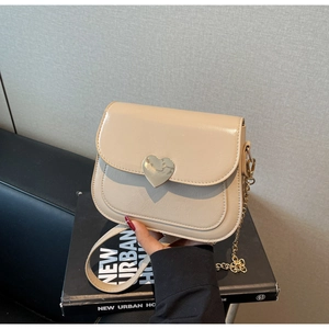 Detail of a beige mini square bag with a gold heart-shaped metal buckle and chain strap