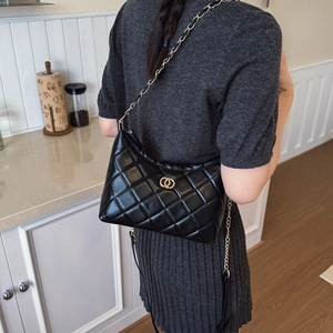 Sac bandoulière matelassé noir avec chaîne dorée présenté dans un décor intérieur