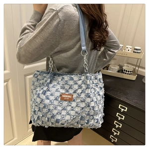Detail of blue checkerboard tote bag with fringe edges and chain strap on shoulder