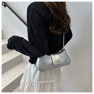 Detail of silver metallic underarm bag with gold buckle on a model in a minimalist setting