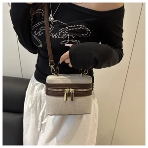 Detail of canvas box bag with brown leather trim and gold zippers on a stylish model