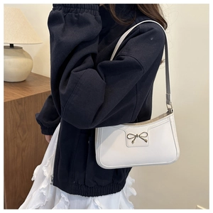 Detail of white PU leather underarm bag featuring a gold metal bow and zipper closure