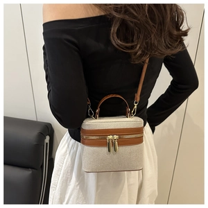 Rear view of model holding canvas and brown leather box bag with contrast stitching