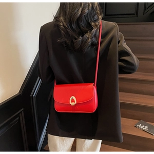Detail of red square crossbody bag with gold arch buckle worn over a black blazer