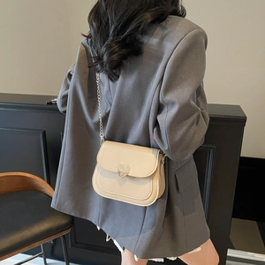 Fashionable beige saddle bag with heart-shaped silver buckle and gold chain strap