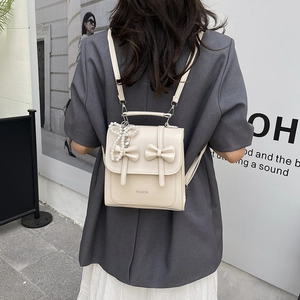 Minimalist cream beige mini backpack with decorative bows and pearl charm in casual outdoor setting