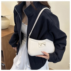 Detail of a white leather underarm bag with a gold bow buckle on a model in a warm setting