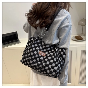 Detail of checkered tote bag featuring frayed edges, leather tag, and metal chain strap