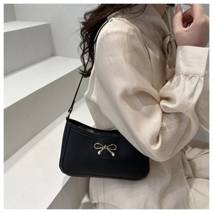 Detail of a black leather shoulder bag featuring a decorative golden bow clasp on the front
