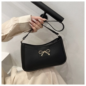 Close-up of black matte leather shoulder bag with a striking gold metal bow decoration