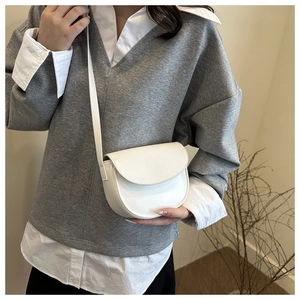 Detailed view of a white minimalist half-moon saddle bag on a model's shoulder