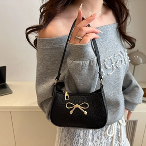 Minimalist black pebble leather underarm bag with a decorative gold metal bow charm