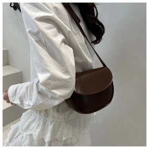 Detail of dark brown saddle bag with smooth leather texture and crossbody strap on model