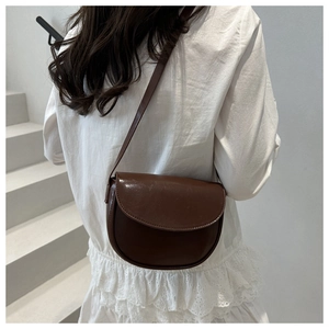 Modern brown saddle bag in polished PU leather worn by a model in a minimalist setting