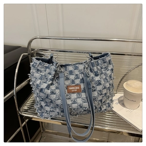Detail of light blue denim tote bag with textured checkerboard pattern and metal chain strap