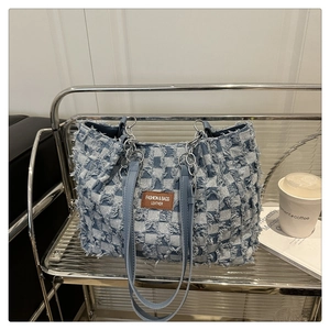 Close-up of checkered denim tote bag with frayed texture, leather tag, and silver chain