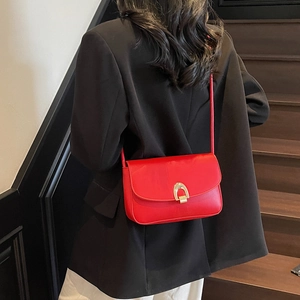 Minimalist red leather square crossbody bag with gold buckle worn by model on shoulder