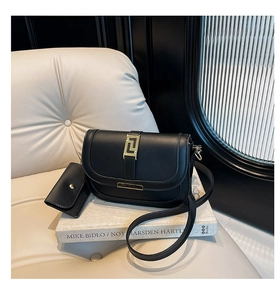Detalle de bolso de silla negro con hebilla dorada y mini estuche sobre libro de arte