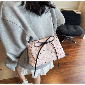 Detail of pink quilted shoulder bag featuring black bow patterns and elegant chain strap