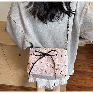 Detail of pink quilted crossbody bag with black bow and silver metal chain strap