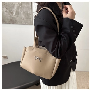 Detail of minimalist beige tote bag with silver bow accent on model's shoulder