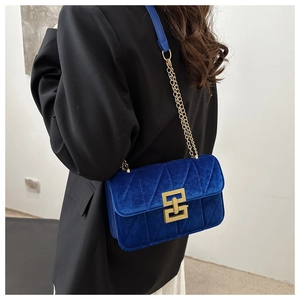 Close-up of klein blue velvet crossbody bag with gold chain and geometric buckle detail