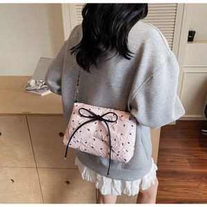 Rear view of a model wearing a pink quilted shoulder bag with large black bows and chain strap