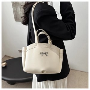 Detail of a beige tote bag with a silver bow accessory worn on a person's shoulder