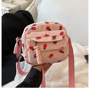 Detail of pink corduroy crossbody bag featuring red strawberry patterns and braided zipper pulls