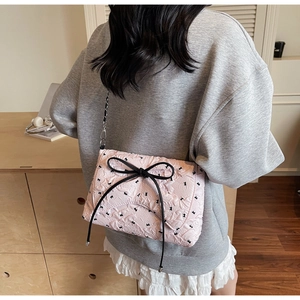 Detail of pink quilted shoulder bag featuring black bows and silver chain strap