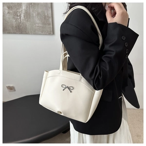 Detail of off-white tote bag featuring a decorative silver metallic bow on smooth leather