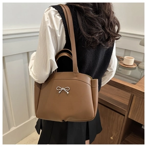 Detail of coffee brown tote bag featuring silver bow buckle and accordion pleat design