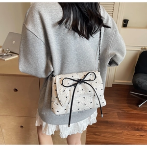 Close-up of white quilted crossbody bag featuring a large black bow and butterfly embroidery