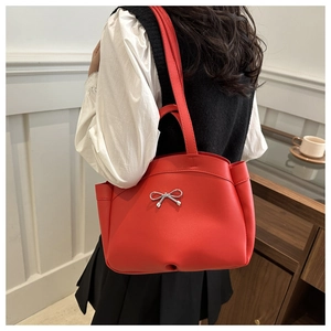 Side view of a red leather tote bag with silver bow ornament worn by a model in interior
