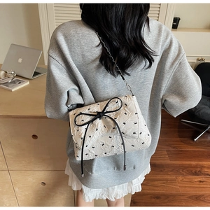 White quilted shoulder bag with black bow and chain strap shown on model's shoulder