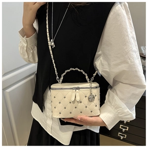 Detail of cream quilted crossbody bag with metal studs and rose-shaped charm