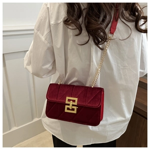 Detail of burgundy velvet crossbody bag featuring quilted texture and golden geometric clasp