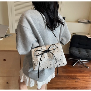 Lifestyle shot of white quilted shoulder bag with large black bow and silver chain strap