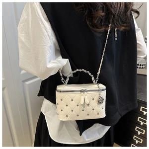 Close-up of white quilted crossbody bag with silver studs and rose charm detail