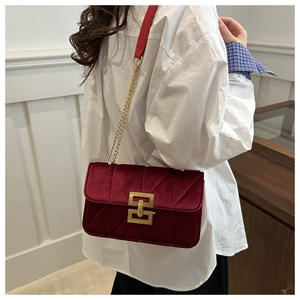 Close-up of wine red velvet shoulder bag with gold geometric clasp on a model