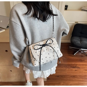 Detail of quilted crossbody bag featuring a black leather bow and rabbit patterns on a model