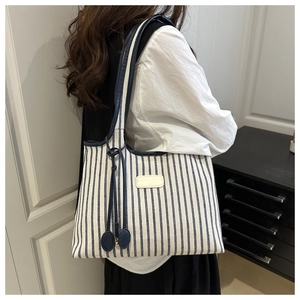 Detail of blue and white striped canvas tote bag with navy leather straps on a model
