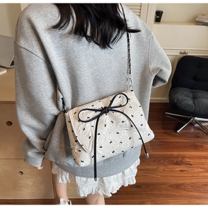 Detail of white quilted crossbody bag with black bow patterns and chain strap on model