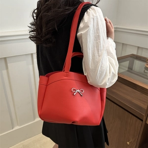 Chic red tote bag with silver metal bow and shoulder strap on model in modern setting