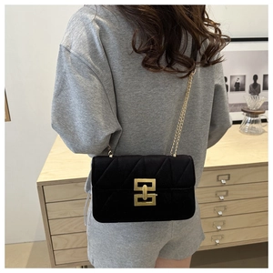 Detail of black quilted crossbody bag with a large geometric gold clasp and chain strap
