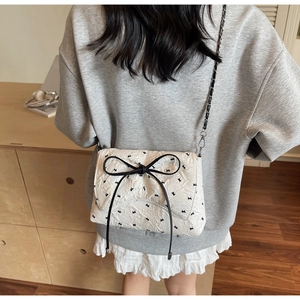 Detail of white quilted crossbody bag with large black bow and silver chain strap