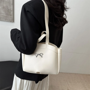 Elegant white leather tote bag with silver bow accent shown in a stylish lifestyle setting